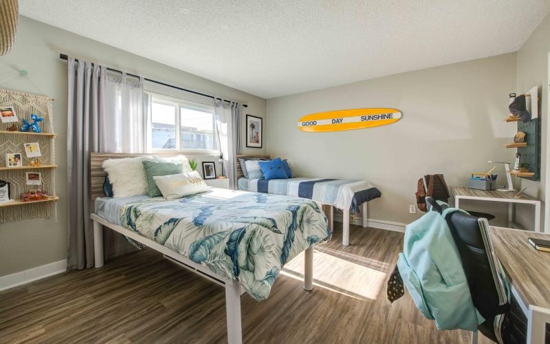 a bedroom with two beds, desks and chairs
